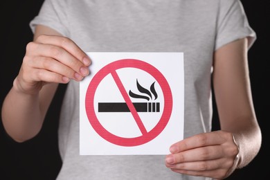 Photo of Woman holding card with no smoking sign on black background, closeup