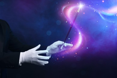 Magician with wand showing trick on dark blue background, closeup