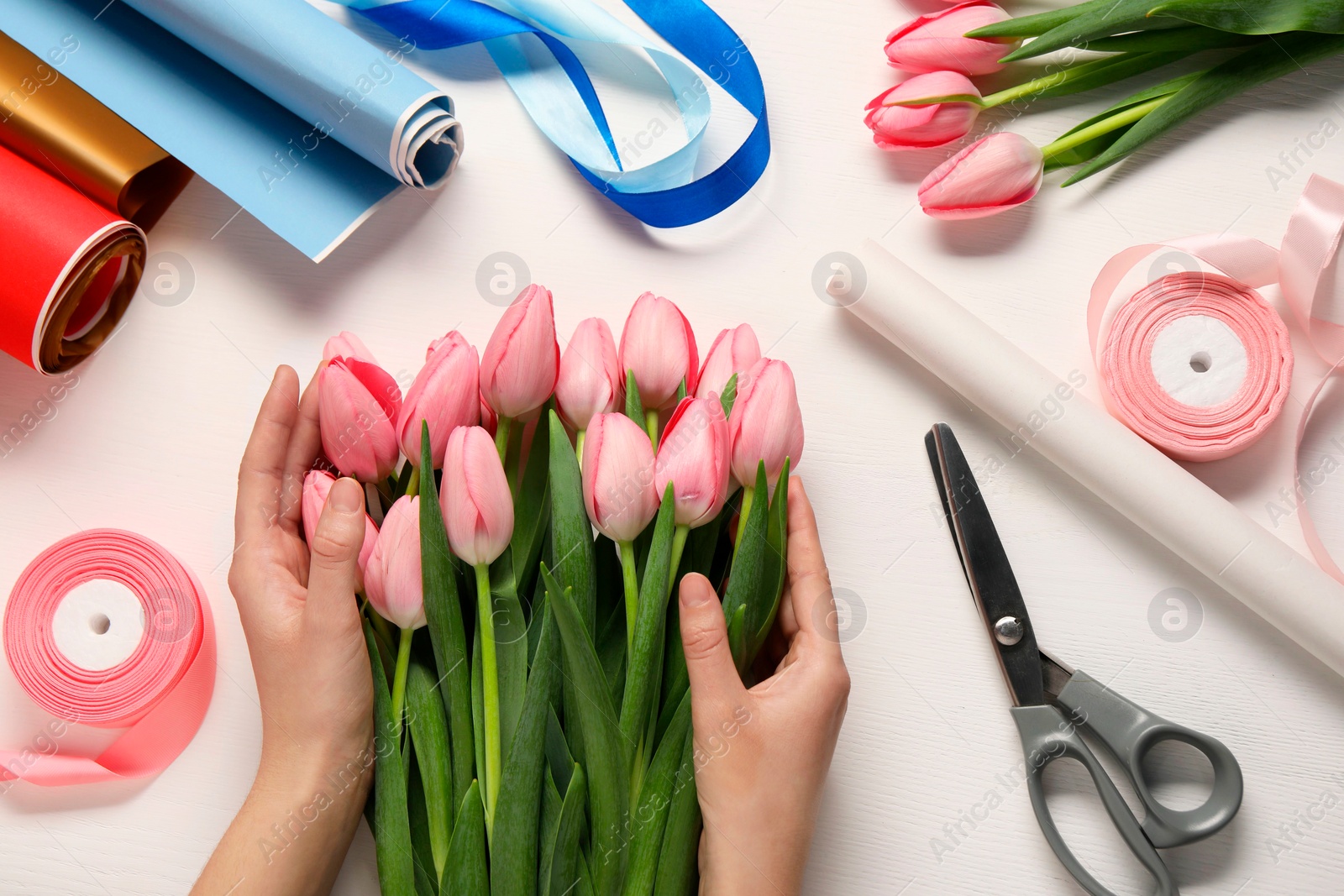 Photo of Woman making bouquet of beautiful fresh tulips at white wooden table, top view