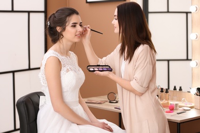 Photo of Professional makeup artist working with young bride in salon