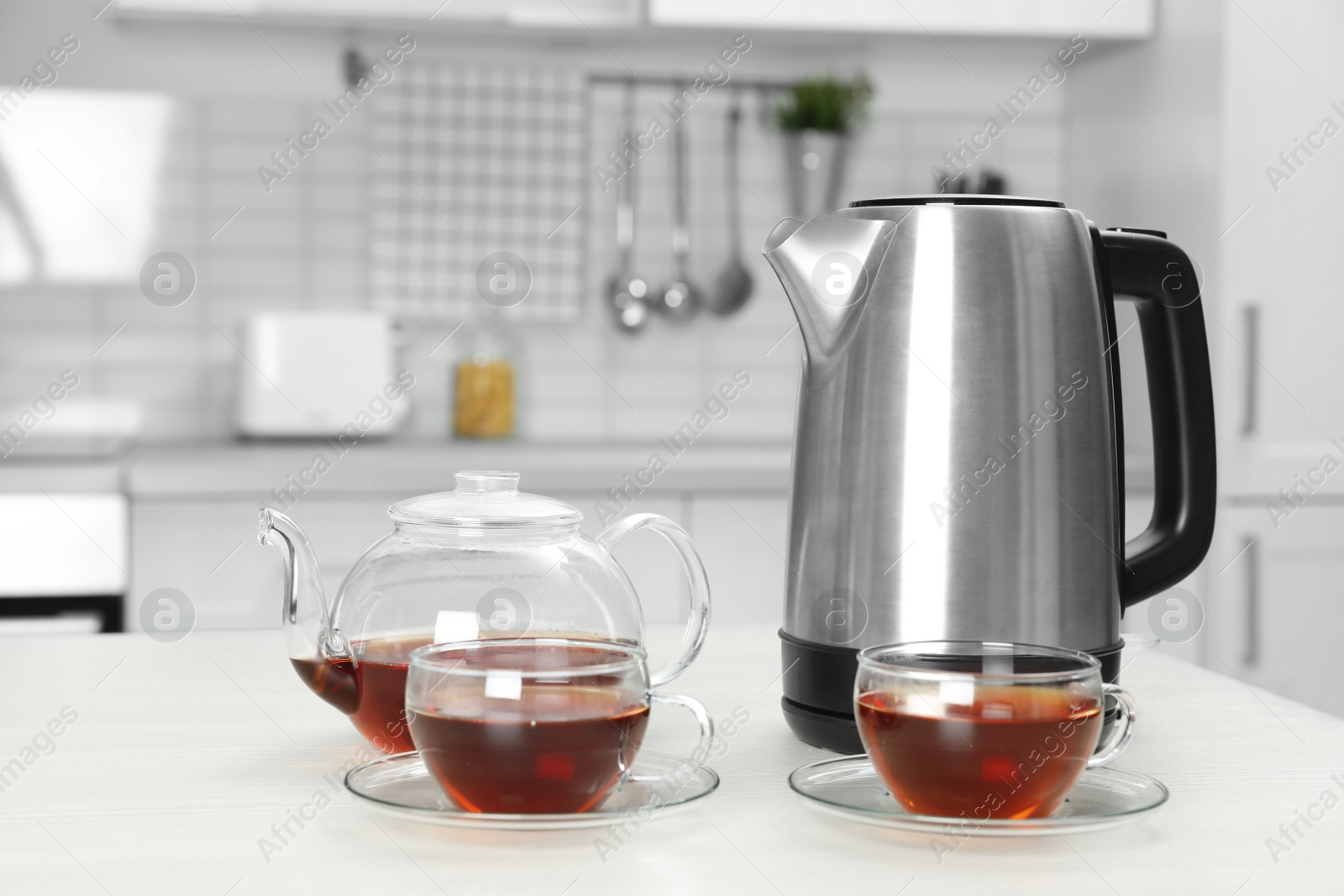 Photo of Modern electric kettle, teapot and cups on white wooden table in kitchen