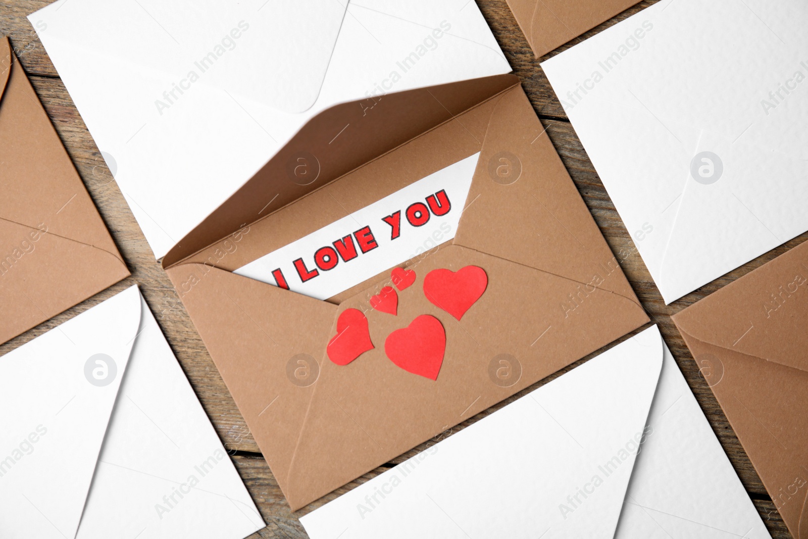 Photo of Sheet of paper with phrase I Love You, envelopes and red hearts on wooden table, flat lay