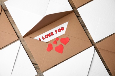 Sheet of paper with phrase I Love You, envelopes and red hearts on wooden table, flat lay