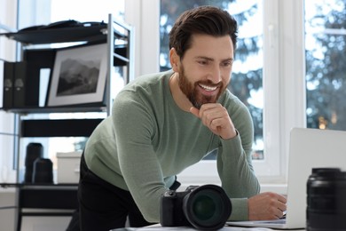 Professional photographer near table with digital camera and laptop in office