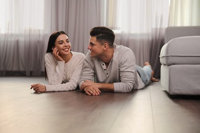 Photo of Happy couple lying on warm floor in living room. Heating system