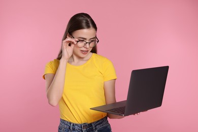 Beautiful woman in glasses with laptop on pink background