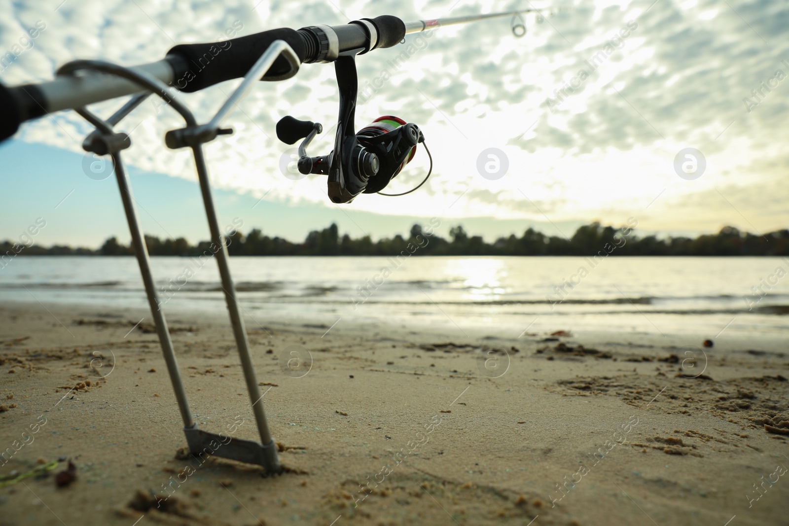 Photo of Fishing rod with reel on sand near river, space for text