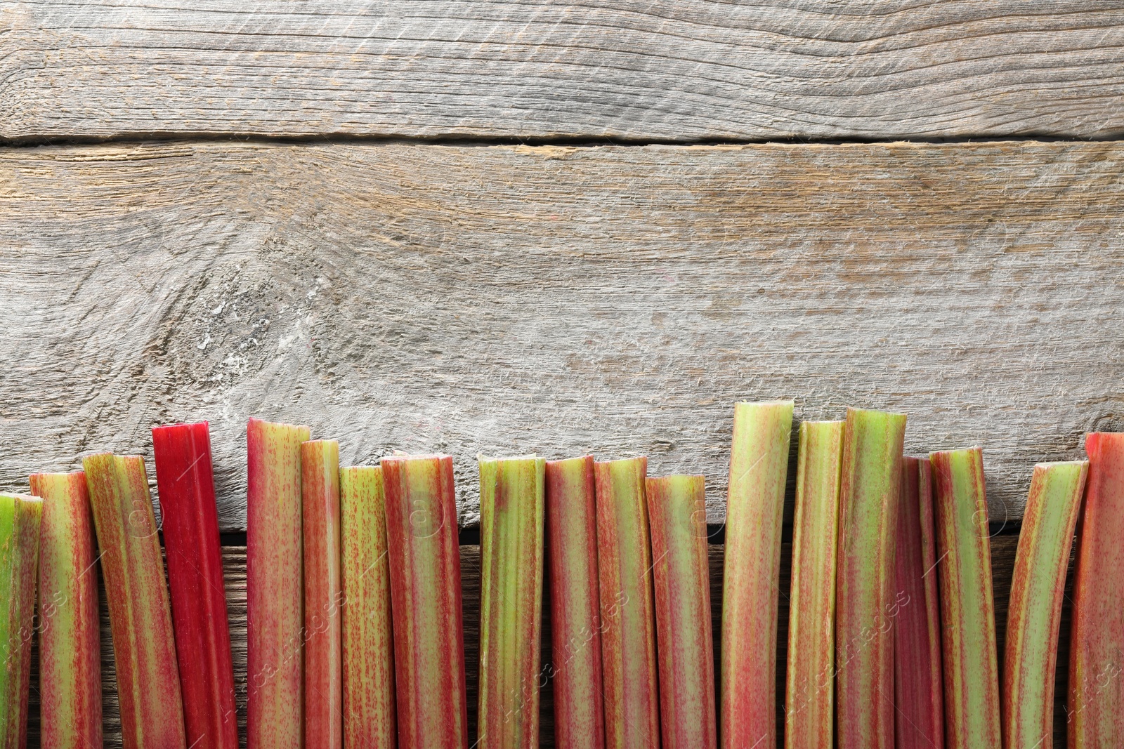 Photo of Fresh rhubarb stalks on wooden table, top view. Space for text