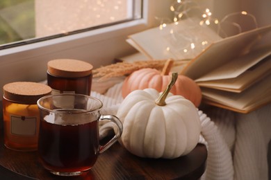 Photo of Cup of hot drink, candles and pumpkins on window sill indoors