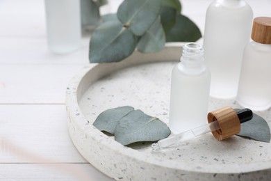 Photo of Bottles of essential oil and eucalyptus leaves on white wooden table, closeup. Space for text