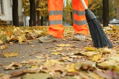 Street cleaner sweeping fallen leaves outdoors on autumn day