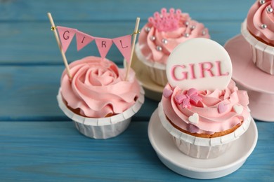 Photo of Delicious cupcakes with pink cream and toppers for baby shower on light blue wooden table