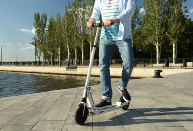 Photo of Man riding modern kick scooter along waterfront, closeup