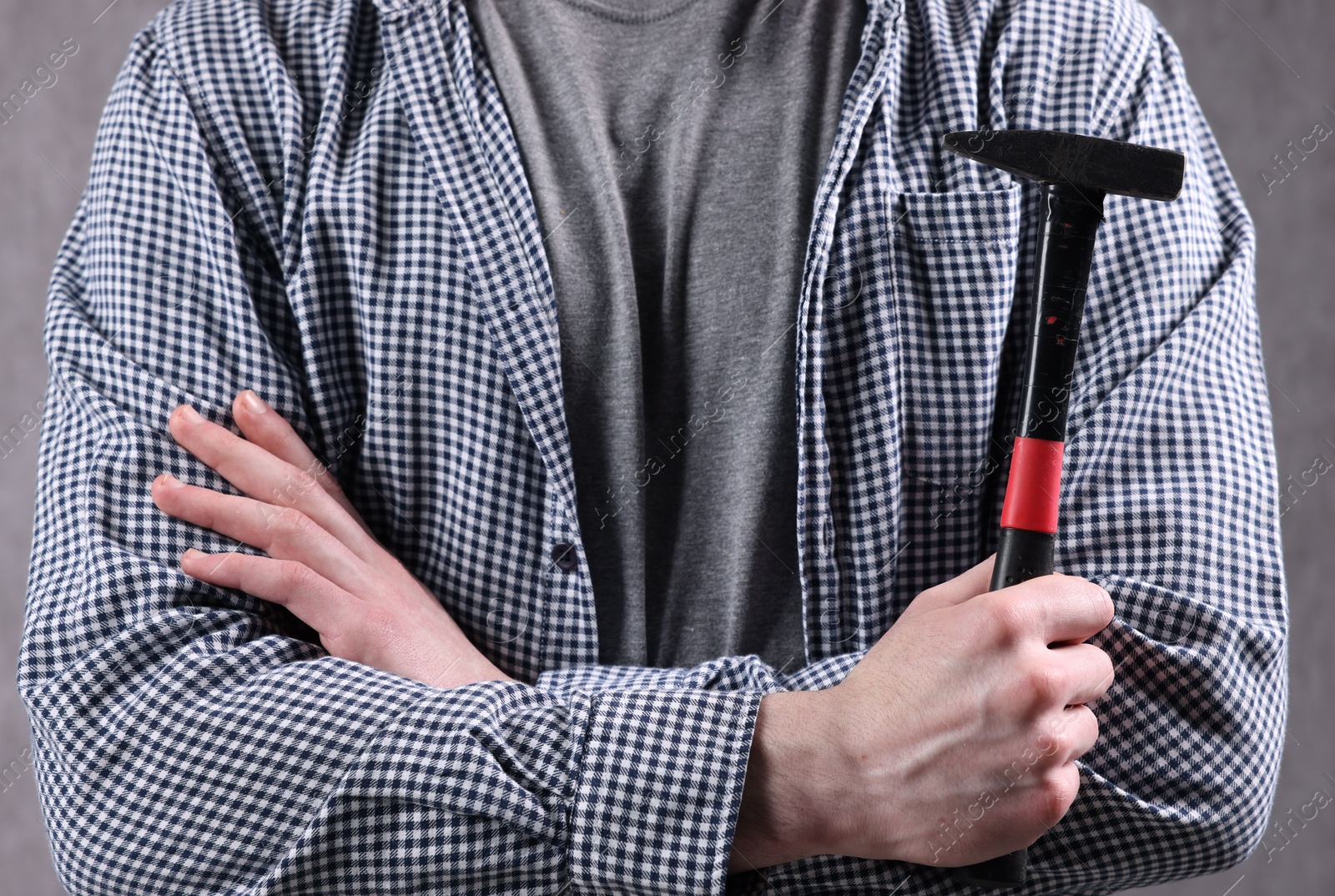 Photo of Young man holding hammer on grey background, closeup
