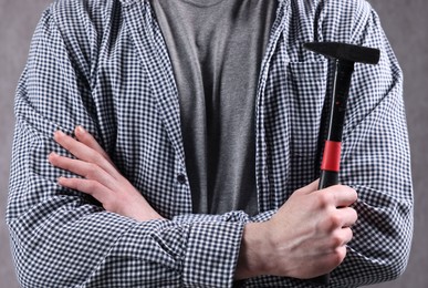 Young man holding hammer on grey background, closeup