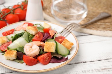 Photo of Tasty salad with croutons, tomato and shrimps served on white wooden table, closeup