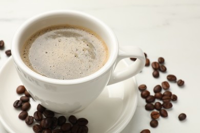 Photo of Cup of aromatic coffee and beans on white table, closeup