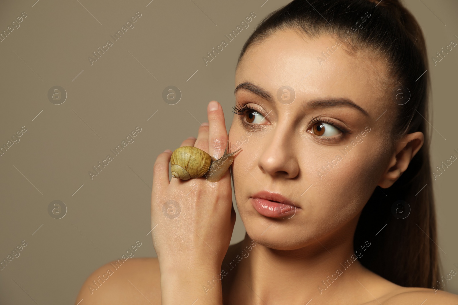 Photo of Beautiful young woman with snail on her hand against beige background