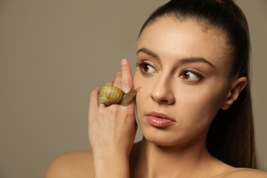 Beautiful young woman with snail on her hand against beige background