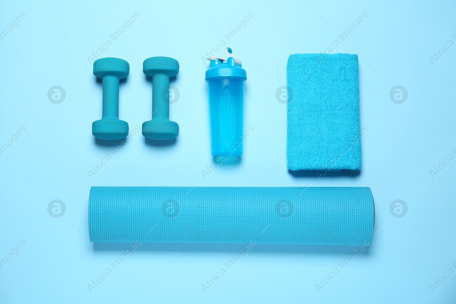Photo of Exercise mat, dumbbells, towel and shaker on light blue background, flat lay