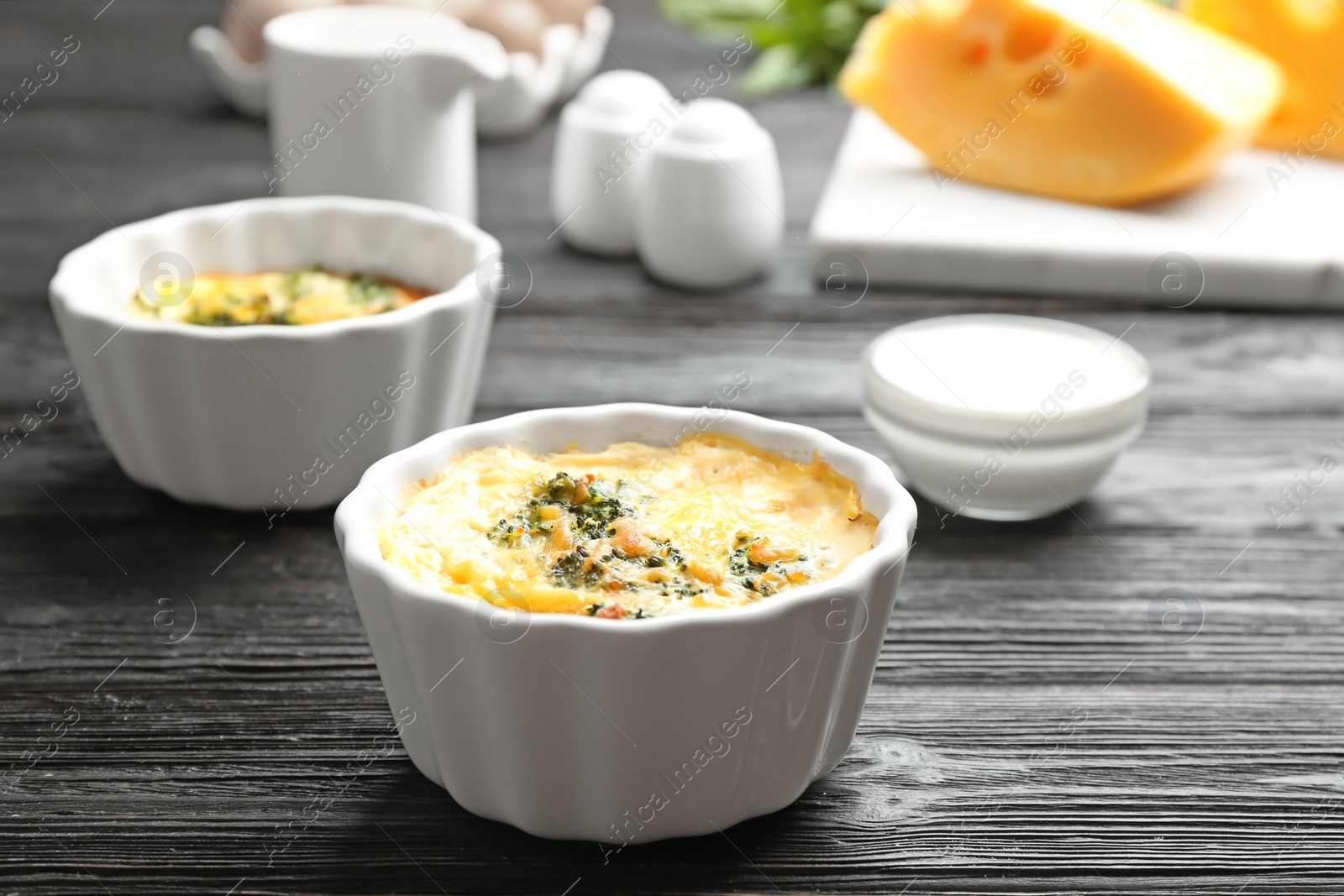 Photo of Tasty broccoli casserole in ramekins on black wooden table