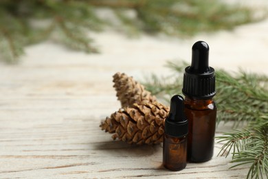 Photo of Glass bottles of essential oil, fir branch and cones on white wooden table. Space for text
