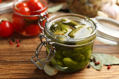 Photo of Glass jar of pickled cucumbers on wooden table, closeup