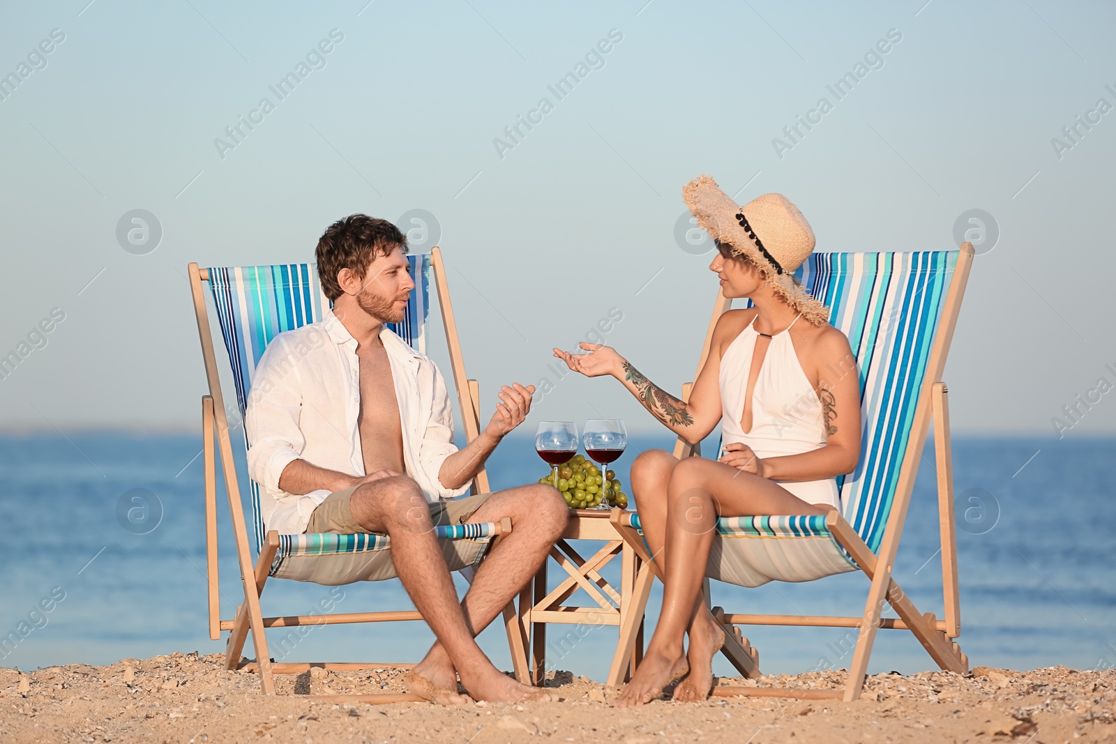 Photo of Young couple having picnic with wine and grapes on beach