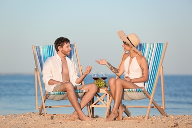 Young couple having picnic with wine and grapes on beach