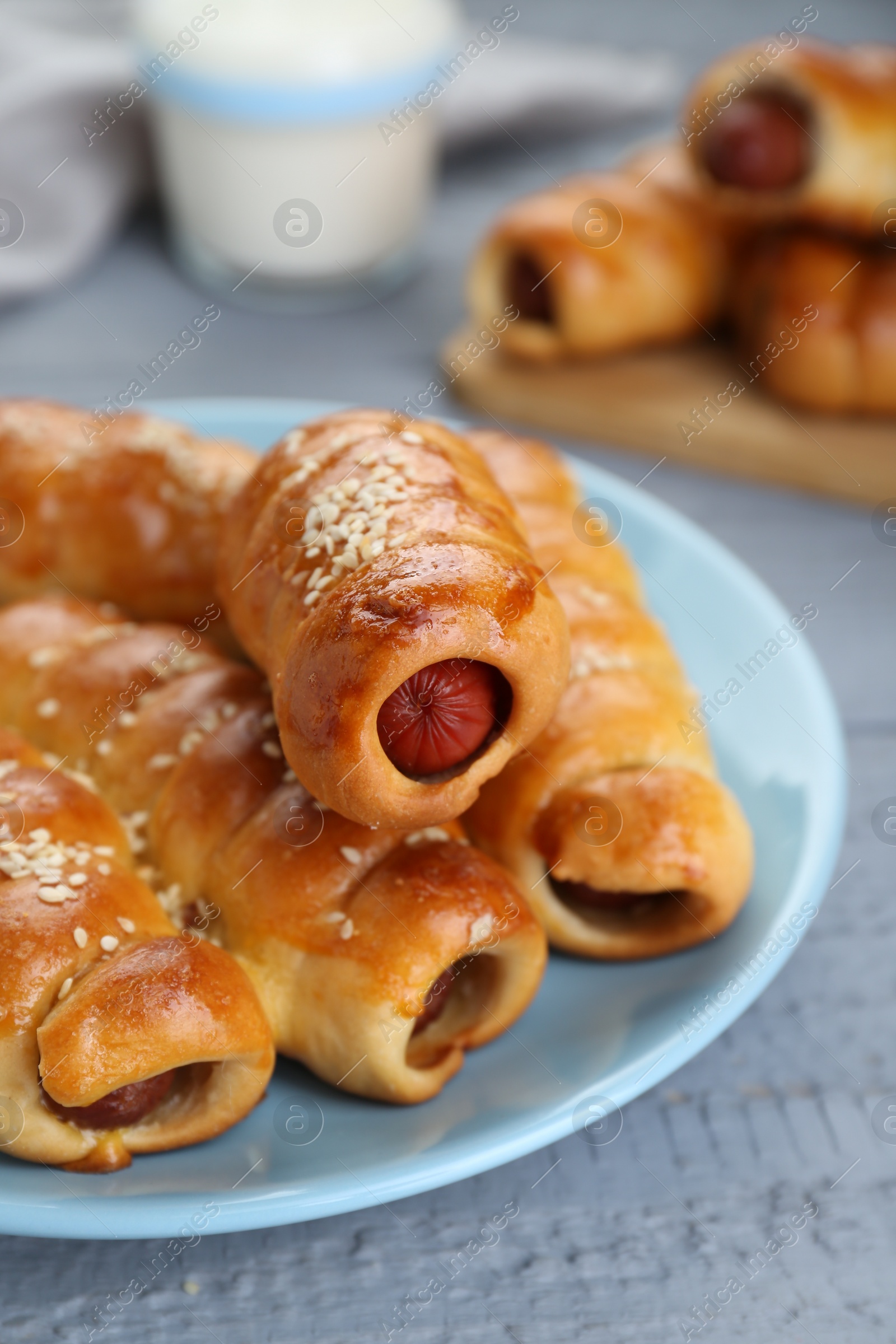 Photo of Delicious sausage rolls and milk on grey wooden table, closeup