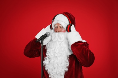 Photo of Santa Claus with headphones and microphone on red background. Christmas music