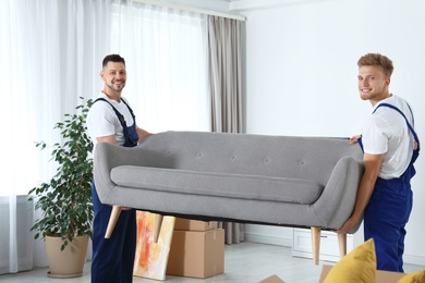 Moving service employees carrying sofa in room