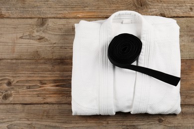 Black karate belt and white kimono on wooden background, top view. Space for text