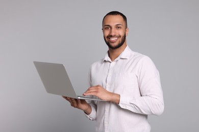 Photo of Smiling young man with laptop on grey background