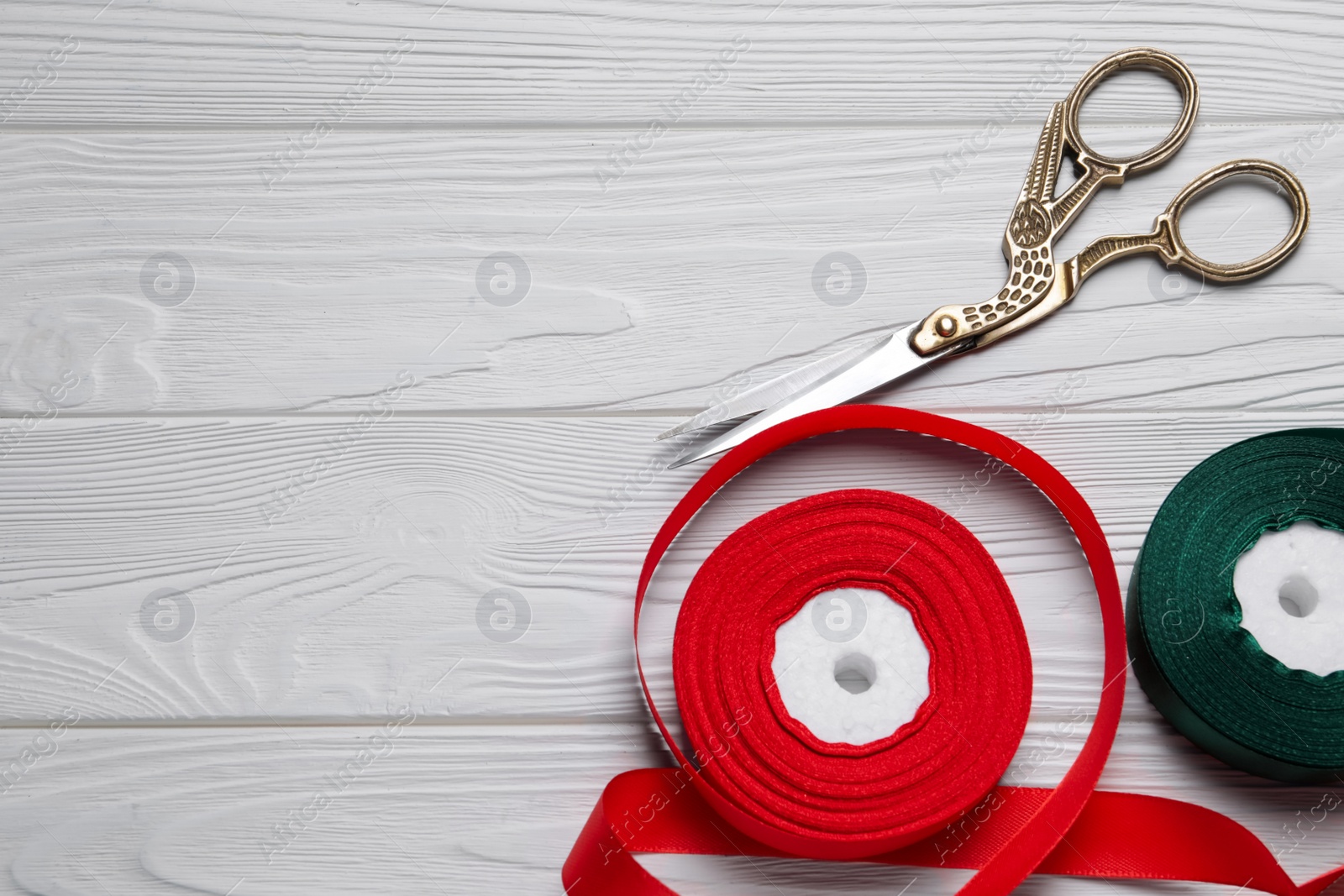 Photo of Pair of scissors with satin ribbons on white wooden table, flat lay. Space for text