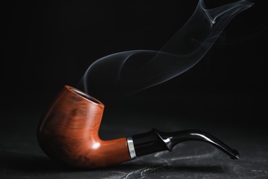 Photo of Stylish tobacco pipe with smoke on black table