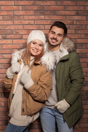 Young couple wearing warm clothes against brick wall. Ready for winter vacation