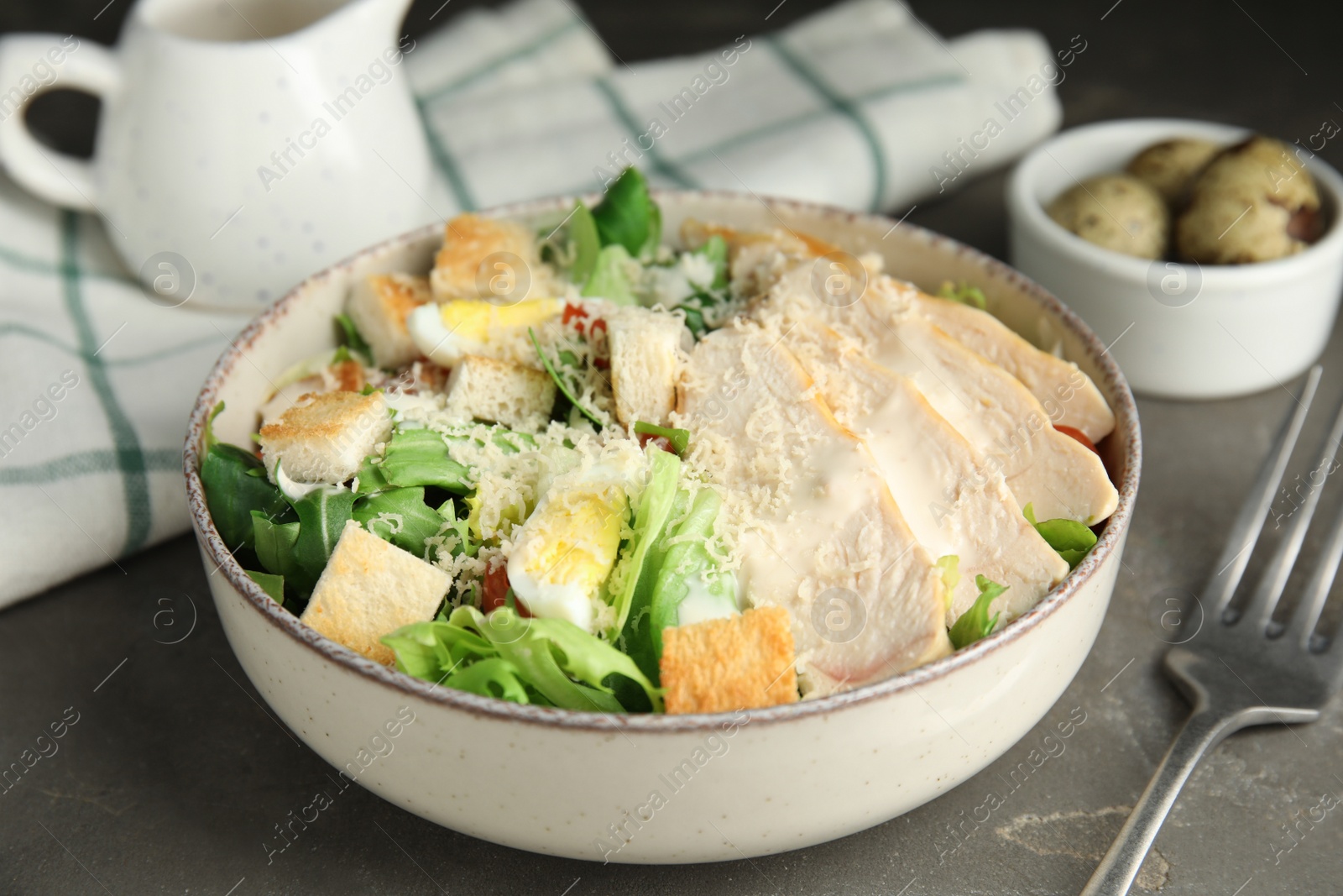 Photo of Delicious Caesar salad in bowl on grey table, closeup