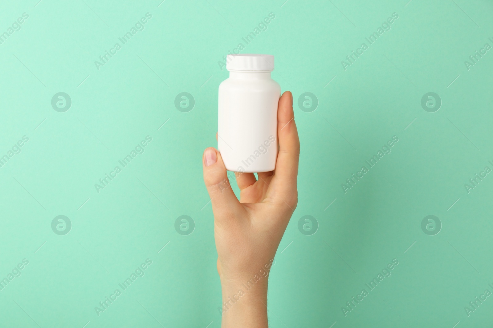 Photo of Woman holding blank white jar of vitamins on turquoise background, closeup. Space for text