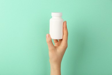 Photo of Woman holding blank white jar of vitamins on turquoise background, closeup. Space for text