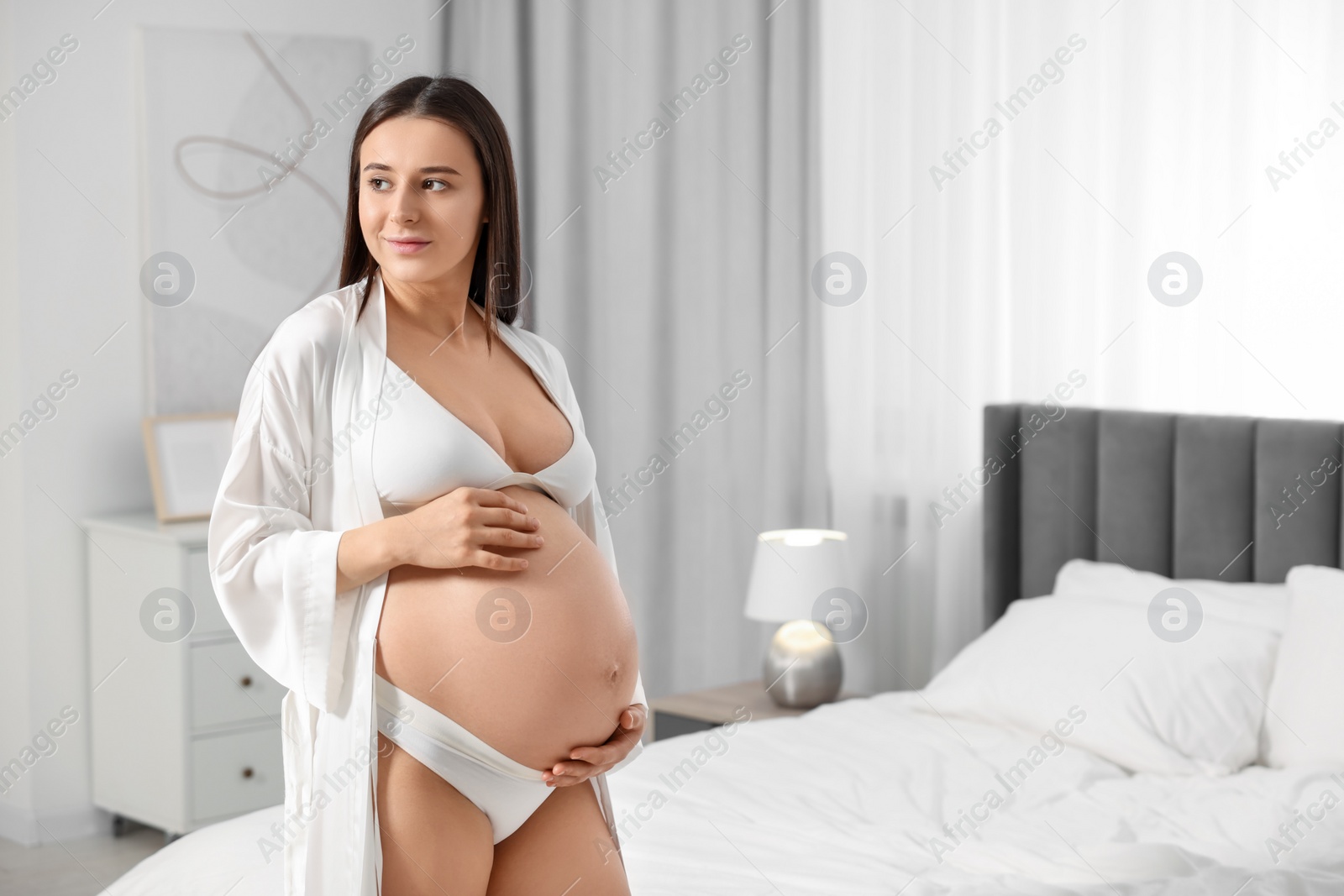 Photo of Beautiful pregnant woman wearing stylish comfortable underwear and robe in bedroom, space for text