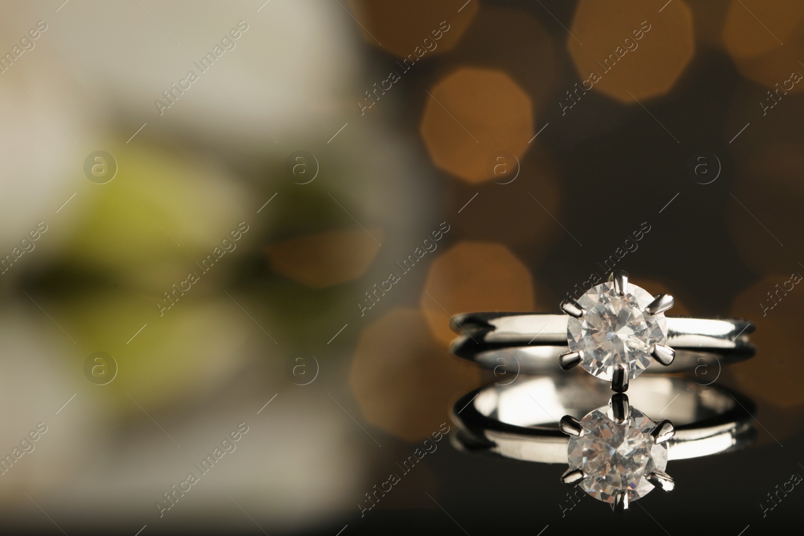 Photo of Beautiful engagement ring against blurred festive lights, closeup. Space for text