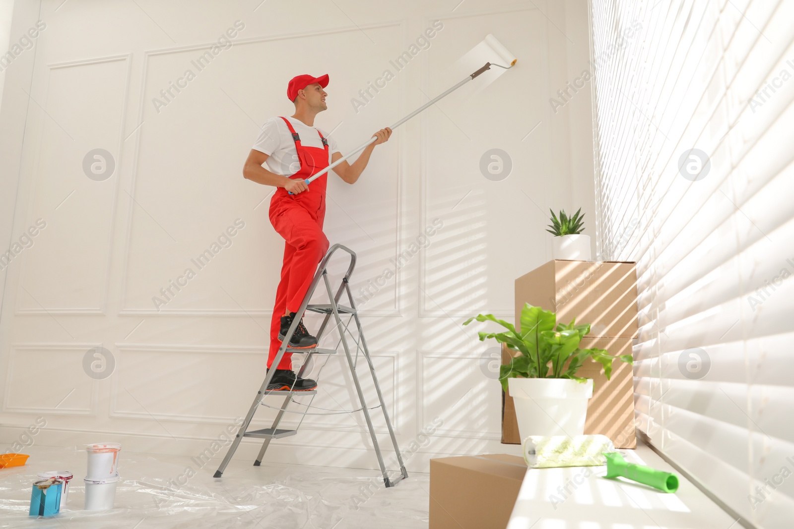 Photo of Worker painting wall with roller on ladder indoors