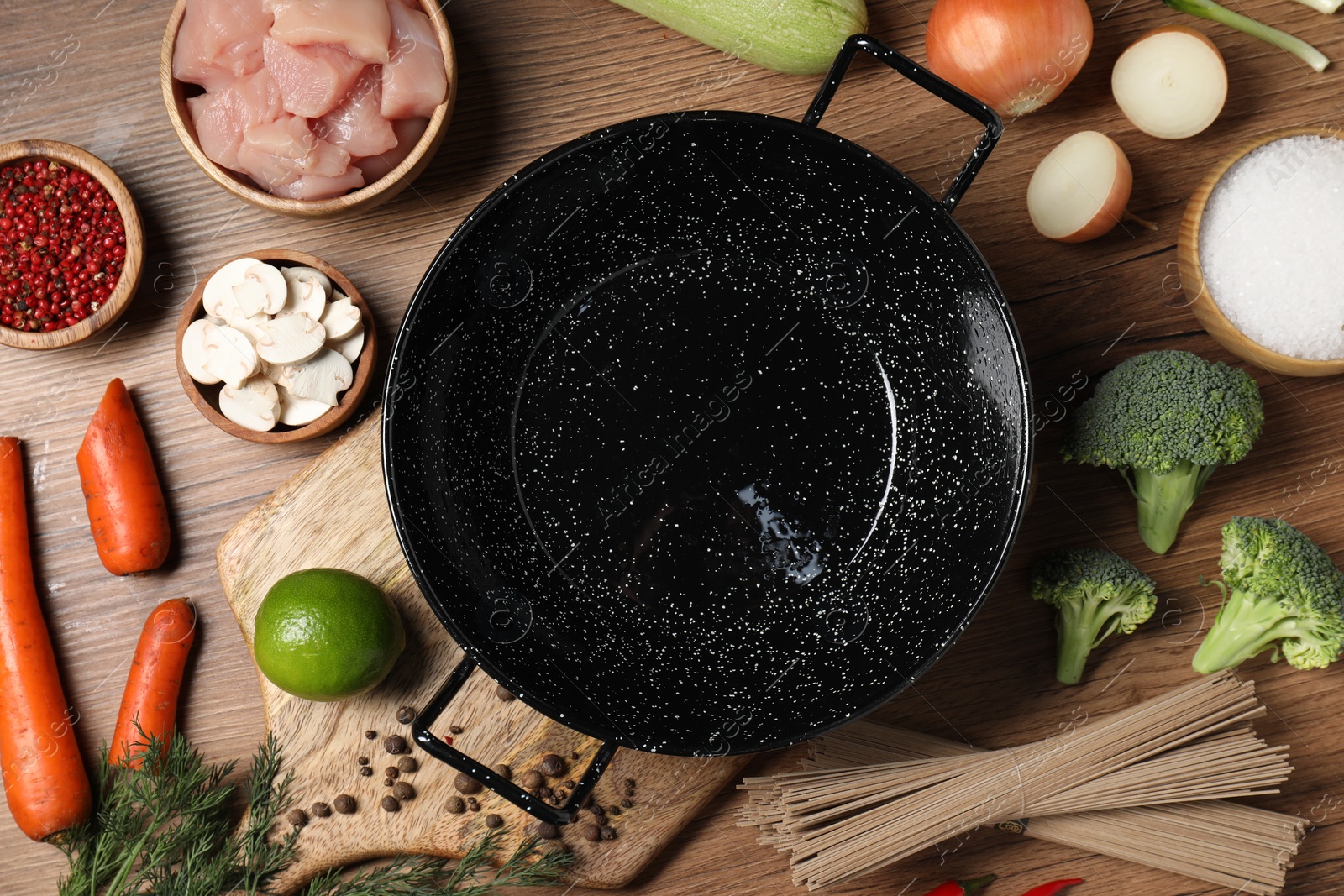 Photo of Empty iron wok surrounded by raw ingredients on wooden table, flat lay