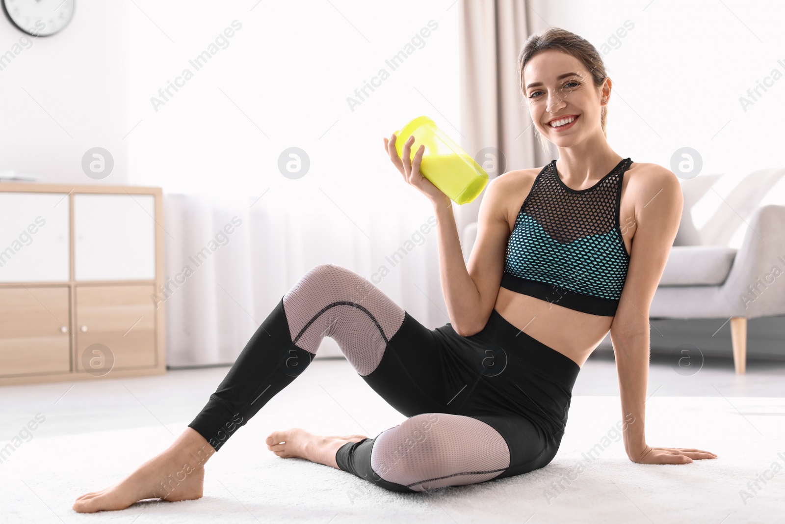 Photo of Young sporty woman with bottle of protein shake sitting on floor at home. Space for text