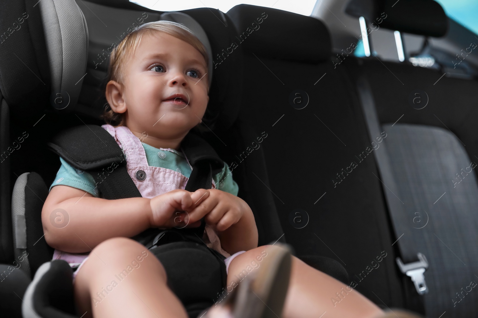 Photo of Cute little girl sitting in child safety seat inside car