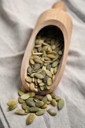 Photo of Wooden scoop with pumpkin seeds on tablecloth, closeup