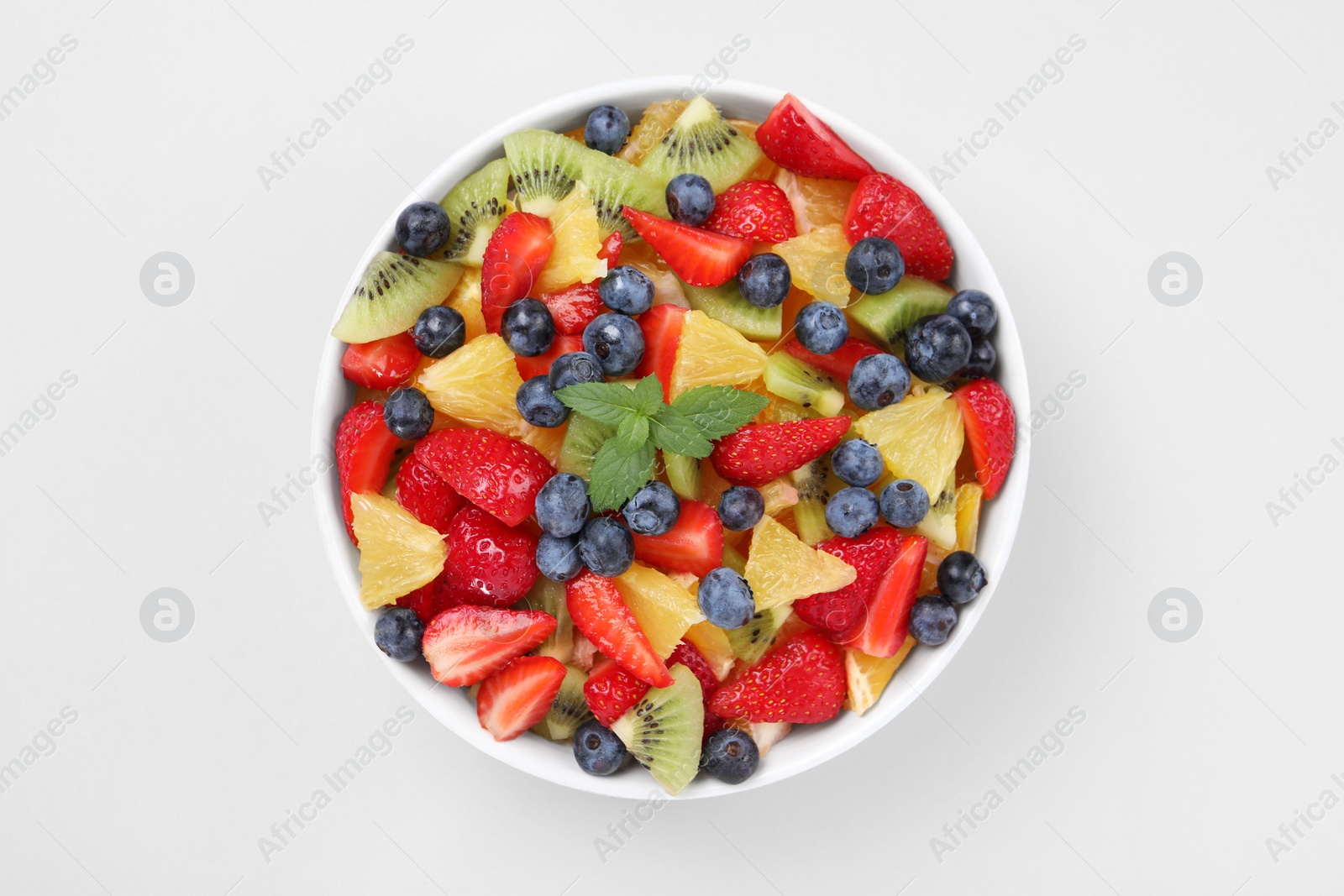 Photo of Yummy fruit salad in bowl on light background, top view