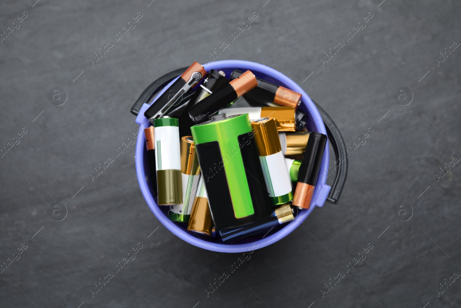 Image of Used batteries in bucket on black table, top view