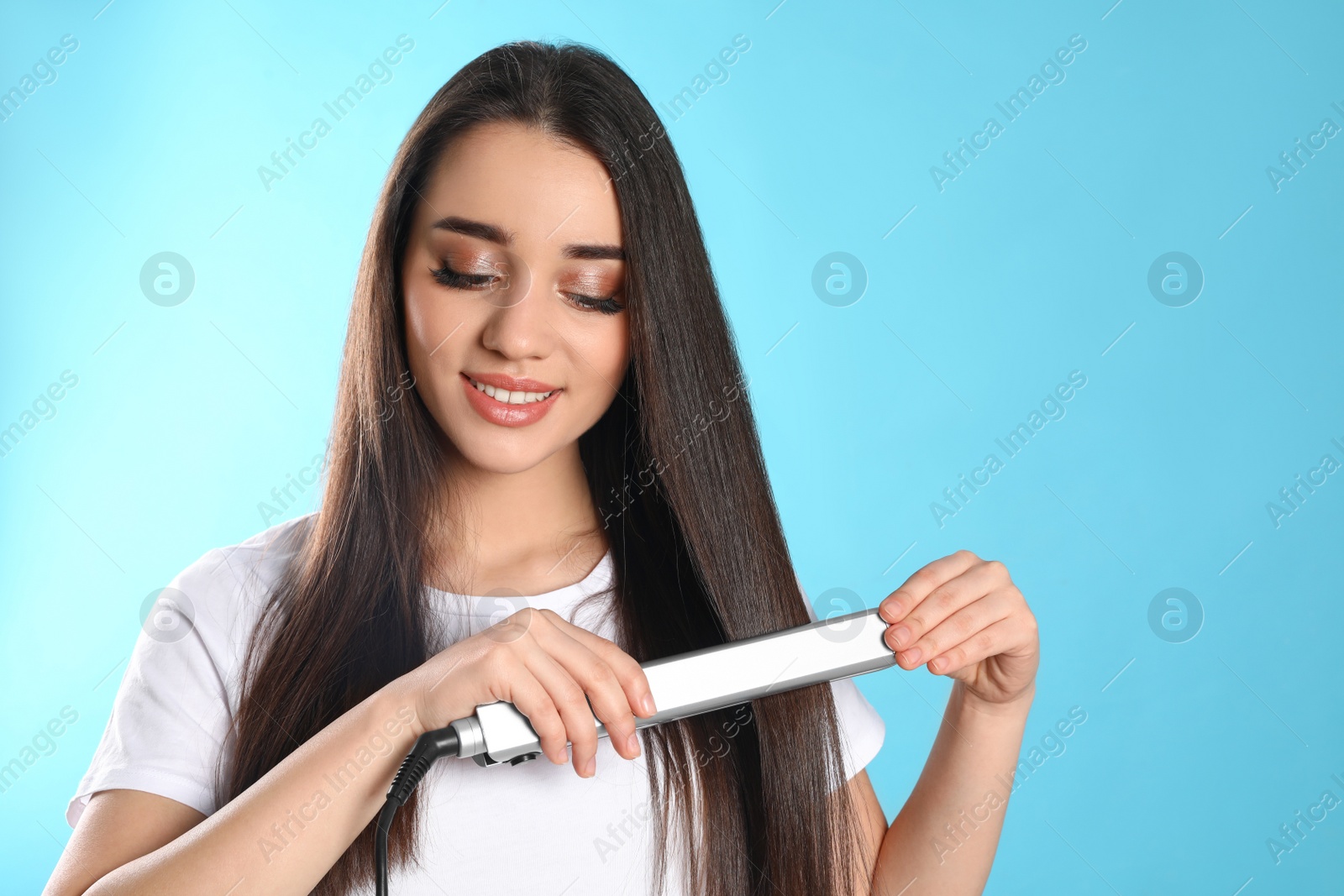 Photo of Happy woman using hair iron on color background. Space for text